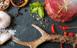 Raw Steak Meat From Roe Deer On The Bridlic Chopping Board With Ingredients As A Sea Salt, Pepper ,basil,chilli And Other. Roe Deer Antler As A Decoration.